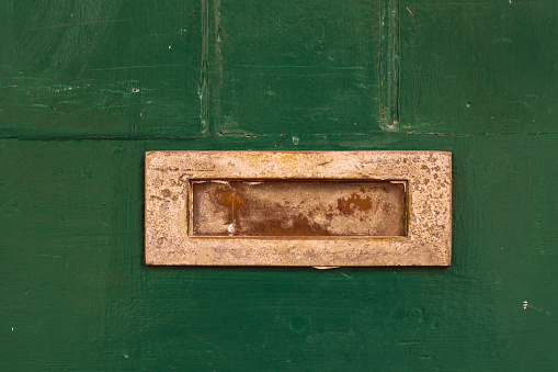 Closeup of an old green wooden front door, with brass mail slot.