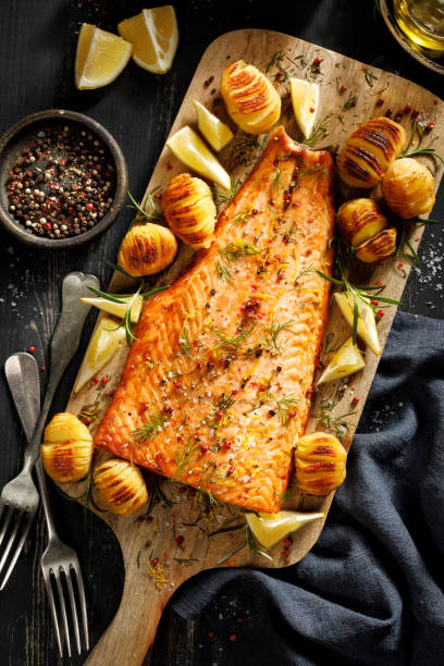 하셀백 감자, 레몬, 신선한 허브를 곁들인 구운 연어 필레가 나무 판에 담겨 있습니다. - salmon cooked pepper plank 뉴스 사진 이미지