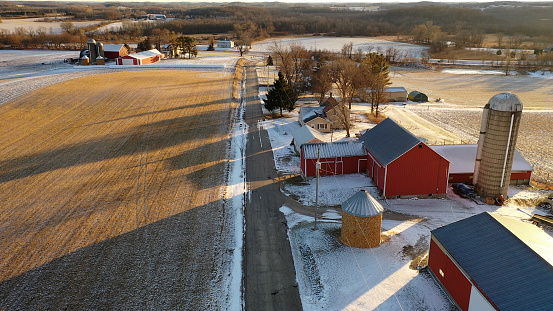Establishing shot of Midwestern countryside in winter.  Aerial view of  rustic road, farm houses, farms along the street. Agricultural field  covered in first snow, sunny, soft sunlight at sunset