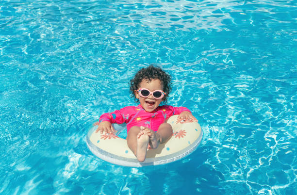 Little girl enjoys the pool Little girl with pink glasses, curly hair and fuchsia swimsuit, enjoys the blue water pool with her round float on a sunny day swimming pool stock pictures, royalty-free photos & images