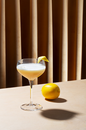 Glass filled with whiskey sour cocktail, lemon on the table