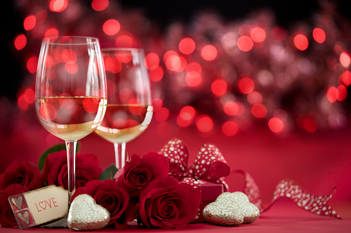 Valentine's Day Red Roses and White Wine with a Gift on a Defocused Lights Background