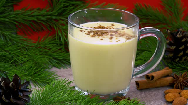 Traditional holiday drink eggnog. sweet drink based on raw chicken eggs and milk. Christmas cocktail with grated nutmeg and cinnamon. background of a spruce branch with cones. xmas drink.