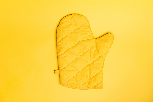 Top view of yellow oven gloves on yellow color background. Mockup for food banner and kitchen protection equipment.