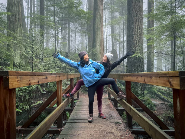 숲에서 다리에 포즈를 취하는 아시아 어머니 과 유라시아 딸 - winter hiking 뉴스 사진 이미지