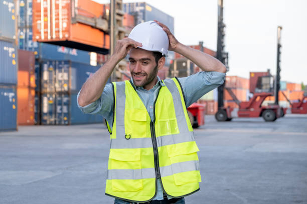 istock Foreman engineer or cargo container worker hold hardhat and stand in front of cranes and stack of shipping 1293848372