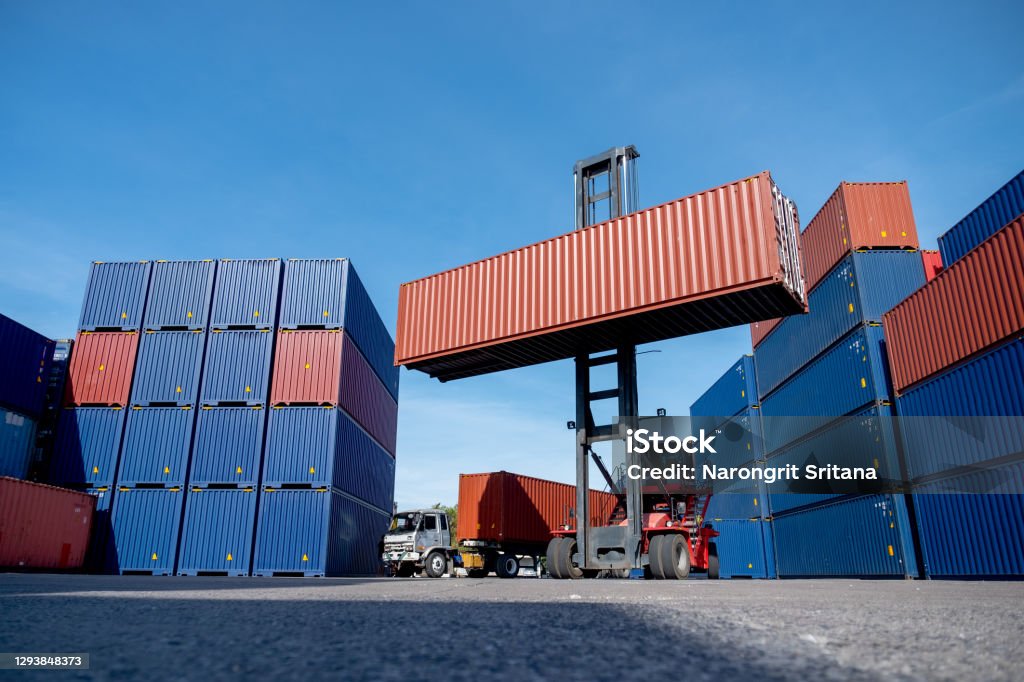 Wide shot of crane truck level up cargo container tank also show stack or layer of containers with different color Wide shot of crane truck level up cargo container tank also show stack or layer of containers with different color, blue and brown with carrier truck as back of crane,  logistic and delivery concept. Cargo Container Stock Photo