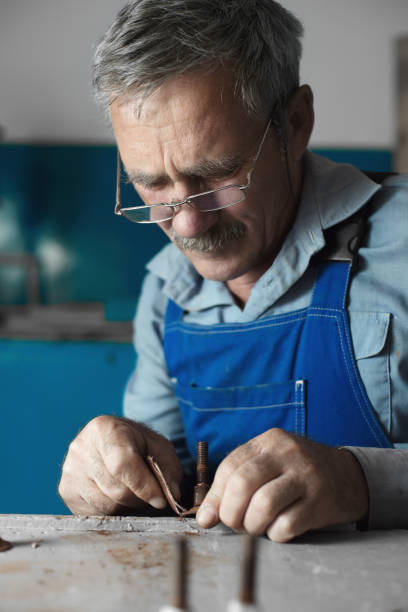 istock An elderly master with glasses at work. A white old man of Caucasian appearance sits at a table and works with his hands 1293849911