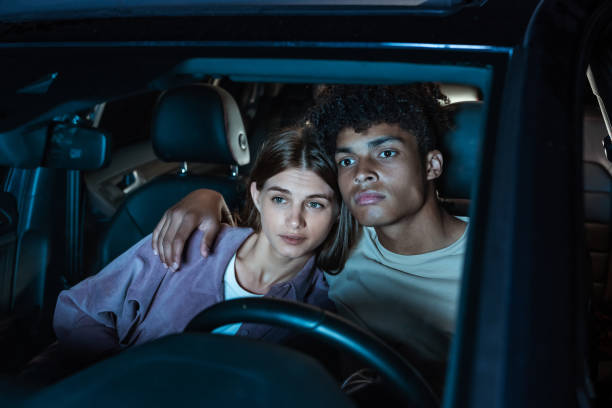 침착하게 즐기십시오. 야외 영화관에서 큰 화면 앞에 주차 된 차에 함께 앉아있는 동안 영화를보는 매력적인 젊은 부부 - drive in movie car inside of billboard 뉴스 사진 이미지
