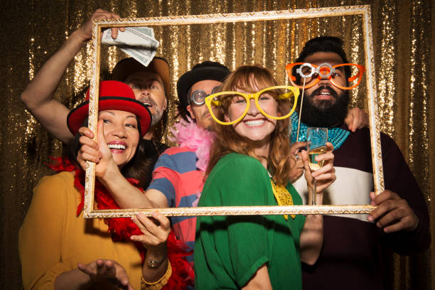 Male and female friends taking funny photo in photo booth Portrait of cheerful male and female friends wearing party props and taking funny photo with picture frame in photo booth. photo booth stock pictures, royalty-free photos & images