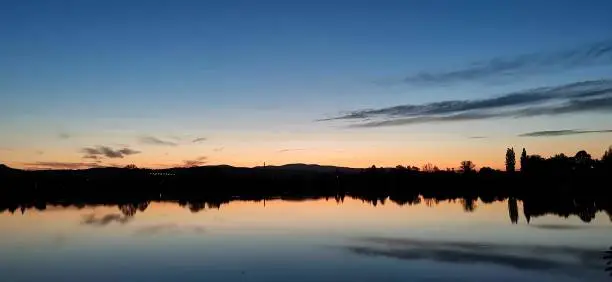 A photo of a lake sunset shot in the middle of the summer. Crickets are chirping and the nature is falling asleep slowly.