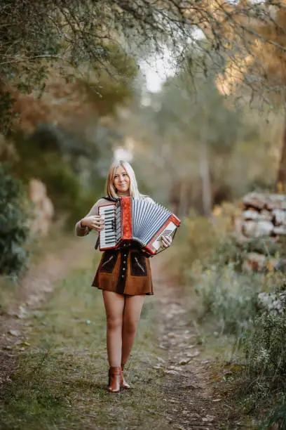 Beautiful young woman playing accordion while walking through a green forest in the Mallorca landscape. Slightly grain added.