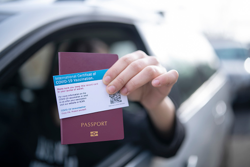 Unrecognisable person in car giving on border control passport and certificate of covid-19 vaccination.