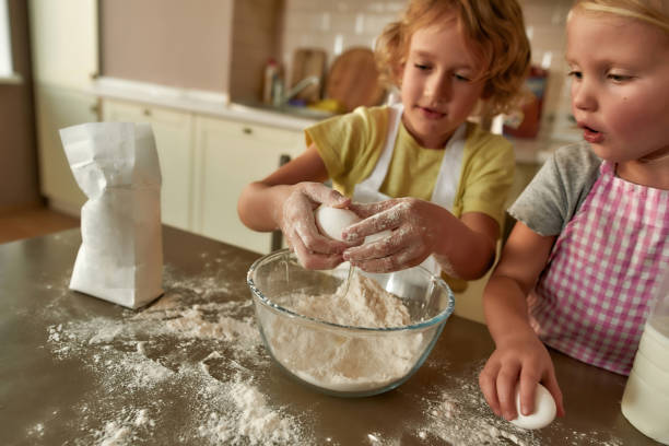 istock Little helpers. Two kids, boy and girl adding eggs and other ingredients while cooking, preparing dough together on the kitchen table at home 1293881175