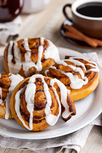 Cinnamon rolls with white icing on a plate and cup of coffee in background