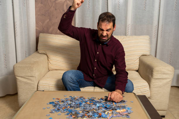 istock Young man with beard sitting on the couch at home doing puzzle 1293886347