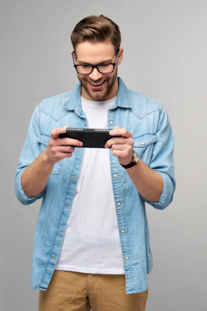 istock Young handcome man playing with portable video game standing over grey background 1293887282