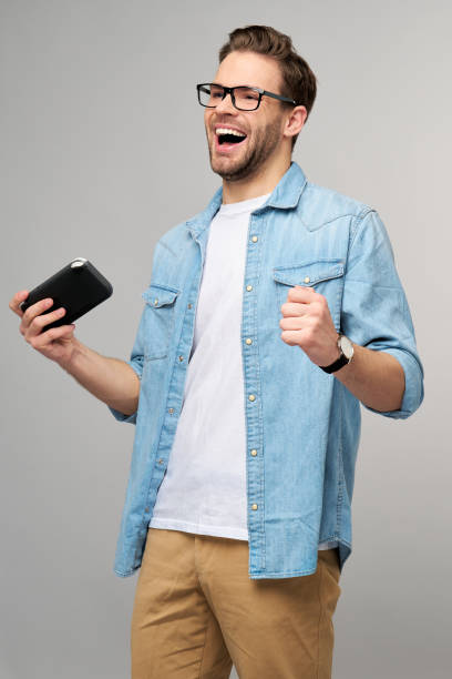 istock Young handcome man playing with portable video game standing over grey background 1293887296