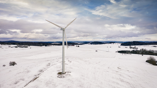 Wind Turbines in white snow covered rural Winter Landscape under sunny winter cloudscape. Green Energy, Alternative Energy Environment Concept Shot. Drone Point of View. Baden Württemberg, Germany, Europe