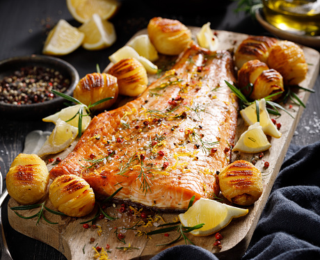 Roast salmon fillet seasoned with herbs and lemon with hasselback potatoes, close-up view