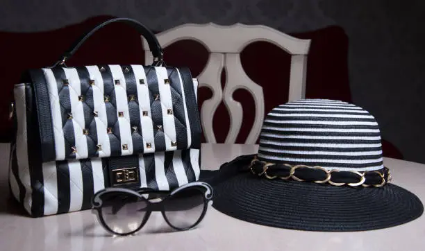 Photo of Striped womenâs hat, black and white purse with stripes and sunglasses on table. Modern fashion style