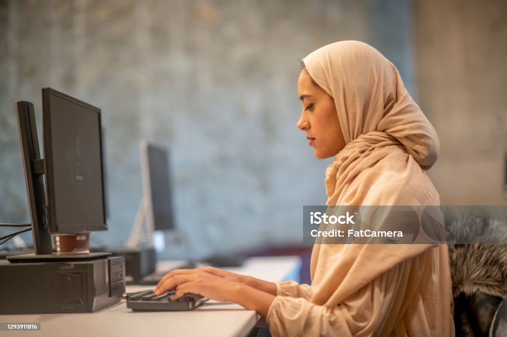 Muslim businesswoman working on computer A Muslim businesswoman wearing a hijab is working on the computer. She is busy typing away to complete her reports. Afghan Ethnicity Stock Photo