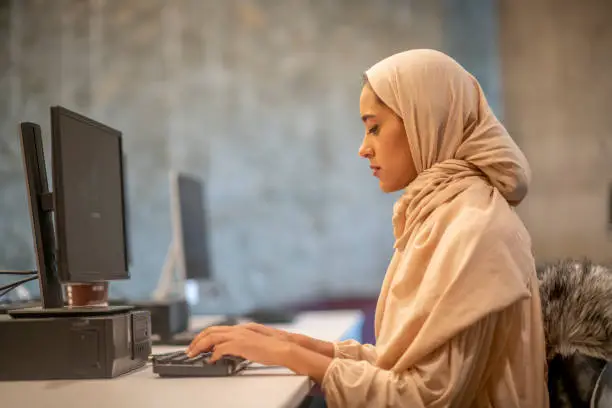 A Muslim businesswoman wearing a hijab is working on the computer. She is busy typing away to complete her reports.