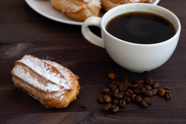 istock homemade vanilla eclairs or profiteroles on a white plate on a wooden table. copy space. Traditional french tasty dessert on dark background. cup of black coffee with beans. 1293921301
