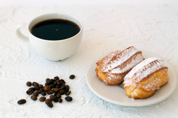 istock Traditional french eclairs on a plate on table. coffee cup with coffee beans on white background. tasty dessert. 1293921338