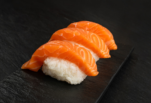 Nigiri Sushi with Raw Salmon Fillet on Black Stone Background Closeup. Thick Pieces of Fresh Red Fish or Trout Susi