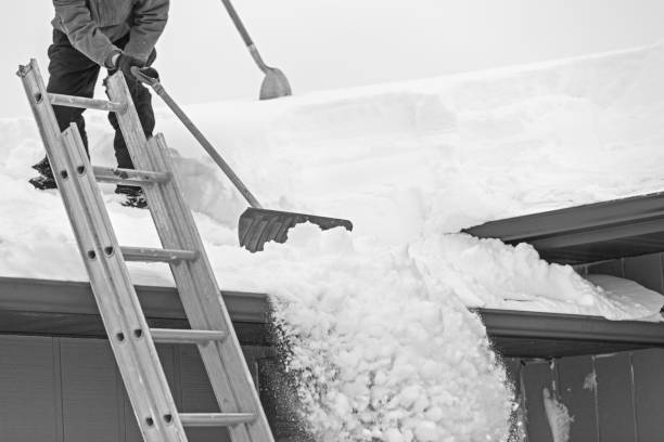 A senior caucasian man is shoveling deep snow off a roof after a blizzard.