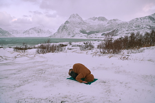 Muslim traveler praying in cold snowy winter day near the car in Scandinavia