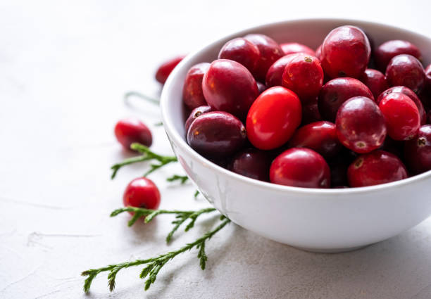 A small white bowl full fresh cranberries on a white textured surface.