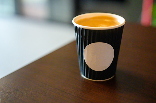 Image of white sticker on paper cup of latte or cappuccino with patterned heart latte art on a wooden table. Concept of serving coffee to take away, coffee to go.