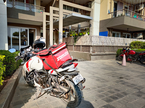 Gurgaon, Delhi, india - circa 2020 : motorcycle rider with red zomato bag delivering food to a urban complex for the fast growing food tech startup unicorn