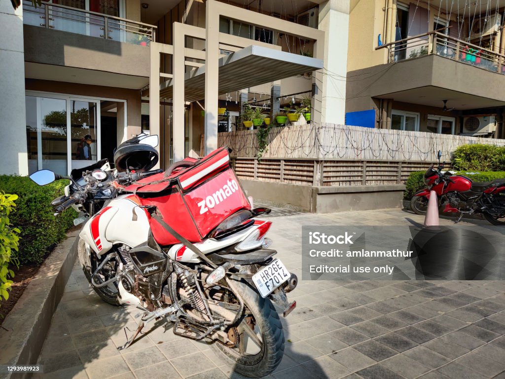 motorcycle rider with red zomato bag delivering food to a urban complex for the fast growing food tech startup unicorn Gurgaon, Delhi, india - circa 2020 : motorcycle rider with red zomato bag delivering food to a urban complex for the fast growing food tech startup unicorn Delivering Stock Photo