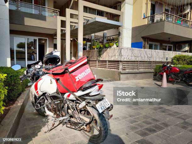 Motorcycle Rider With Red Zomato Bag Delivering Food To A Urban Complex For The Fast Growing Food Tech Startup Unicorn Stock Photo - Download Image Now