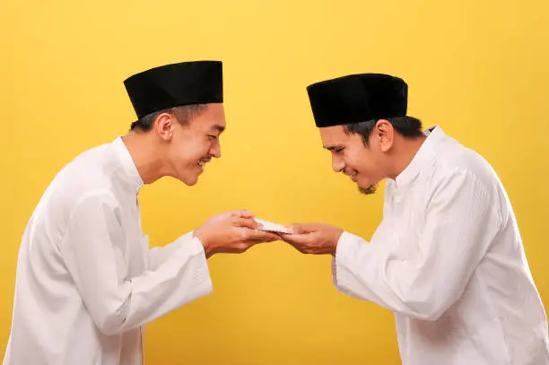 Young Asian Muslim man give alms to other muslim on Ramadan Kareem. It's the best time to give alms to everyone need, isolated on yellow background