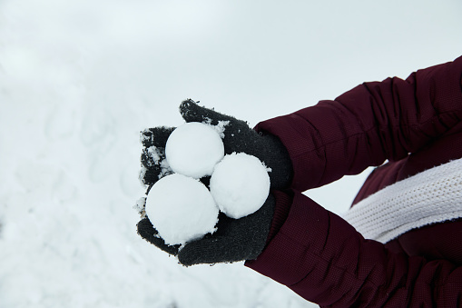 Snowballs on the hands in gray gloves on the white snow background.