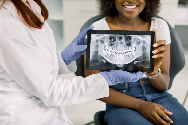 Close up cropped image of female dentist and african american woman patient at dentist's office, holding together digital tablet with patient xray panoramic jaw and teeth image. Oral care and check up Close up cropped image of female dentist and african american woman patient at dentist's office, holding together digital tablet with xray panoramic jaw and teeth image. Oral care and check up tablet pc and digital hospital tools stock pictures, royalty-free photos & images