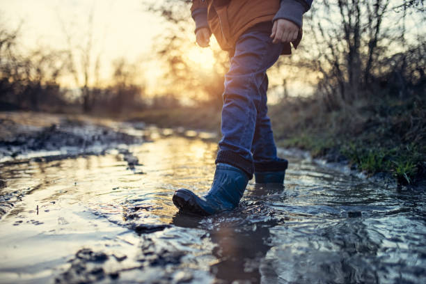 Little boy walking in muddy puddle on winter day.