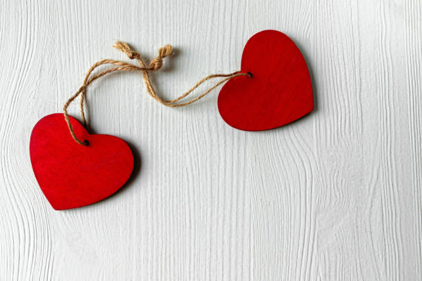 istock Two red hearts knotted together touching each other on a white wooden table, with copy space on the lower left corner 1294005901