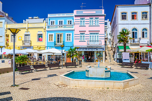 Lagos, Portugal, June 18, 2017: historical town centre with colorful multicolored buildings houses, fountain and benches in sunny summer day, blue sky background