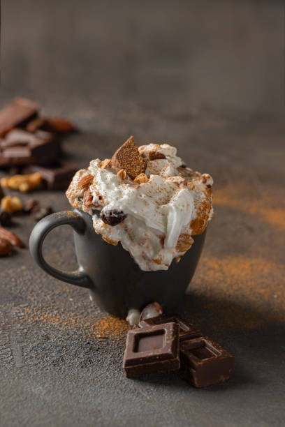 istock Hot chocolate cocoa cup with whipped cream decorated with cinnamon, chocolate slice and nuts  on concrete background. Traditional beverage for cold days concept. 1294011614