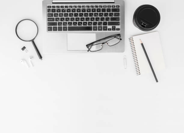 istock Workplace in the office with a white desk. Top view from above of keyboard with notebook,pencil,eyeglasses and coffee. Space for modern creative work of designer. Flat lay with copy space. Business and finance concept. 1294011755