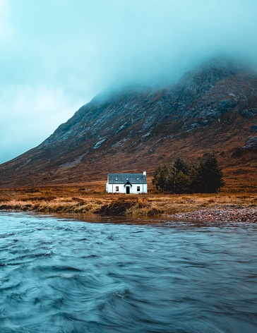 Beautiful white cottage in Glencoe, Scottish Highlands. Mountain on the background and river in foreground.