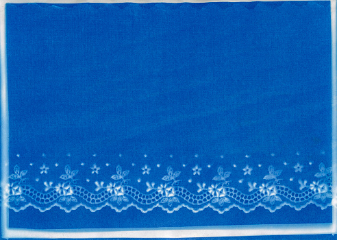 Cyanotype print of machine made eyelet lace border edging in a floral pattern.