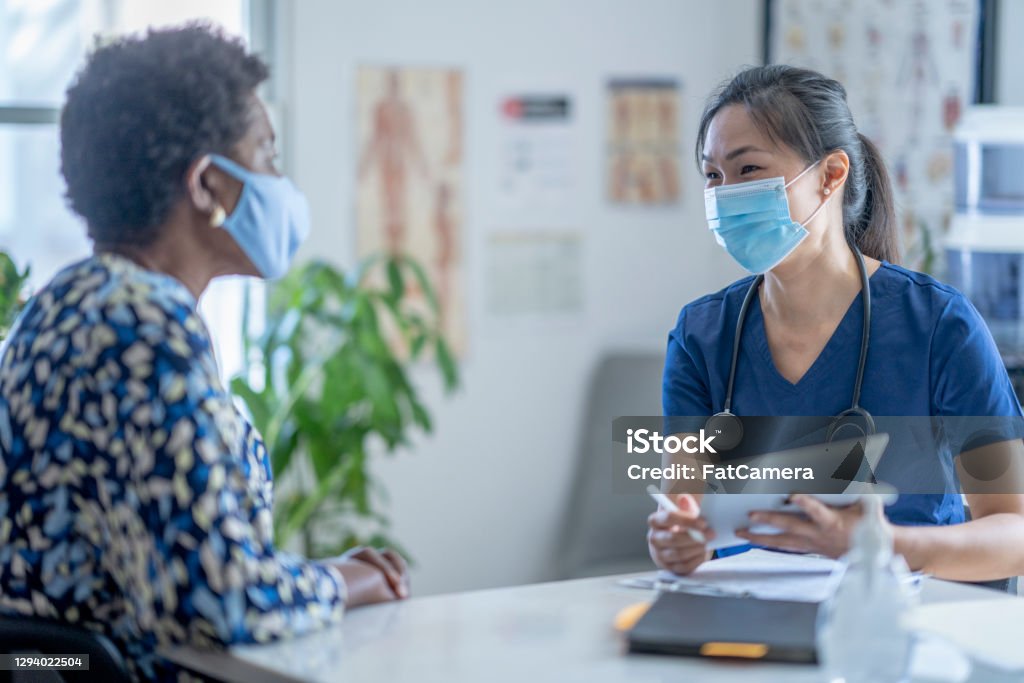 Asian Female doctor meeting patient An Asian female doctor meets with her patient at her medical office. They are both wearing a face mask to prevent the transfer of germs during the coronavirus pandemic. Patient Stock Photo