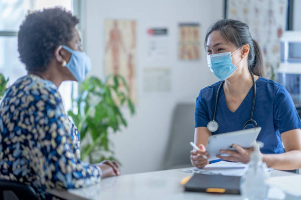 Asian Female doctor meeting patient An Asian female doctor meets with her patient at her medical office. They are both wearing a face mask to prevent the transfer of germs during the coronavirus pandemic. female nurse photos stock pictures, royalty-free photos & images