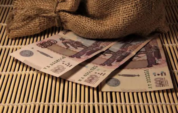 A sack of burlap stands on paper money. 500 rubles of Russian money. Money on a bamboo carpet.